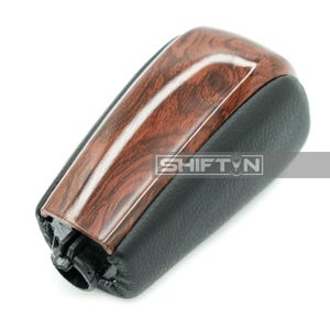 May include: A car gear shift knob with a wood grain top and black leather base. The wood grain has a glossy finish. The text "SHIFT N" is printed on the side of the knob.