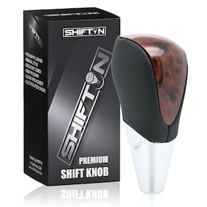May include: A premium shift knob with a black leather top and a wood grain finish. The knob has a chrome base and is next to a black box with the text "SHIFT'N" and "PREMIUM SHIFT KNOB".