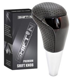 May include: A black and silver premium shift knob with a perforated leather top and a glossy black accent. The shift knob has a chrome base and is next to a black box with the text "SHIFT N PREMIUM SHIFT KNOB".