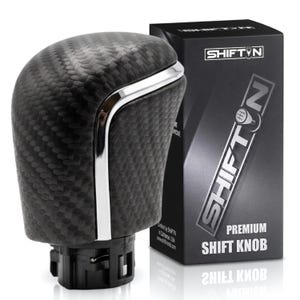May include: A black carbon fiber textured shift knob with a silver chrome trim accent, positioned next to a black rectangular product box labeled SHIFTN PREMIUM SHIFT KNOB with a graphic of a gear shift pattern on the letter O.