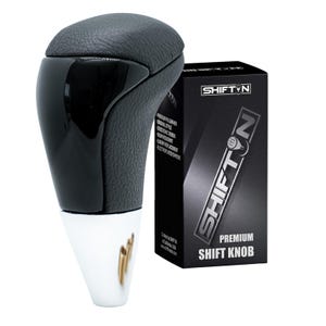 May include: A black and silver shift knob with a leather top and a glossy black front. The shift knob is next to a black box with the text "SHIFTYN" and "PREMIUM SHIFT KNOB".