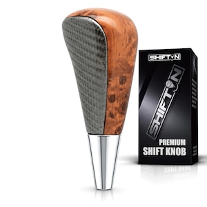 May include: A gear shift knob featuring a polished chrome base, a textured dark gray carbon fiber-style front panel, and a smooth brown burl wood-grain back. Next to it is a black box labeled SHIFTON PREMIUM SHIFT KNOB with a gear pattern logo.