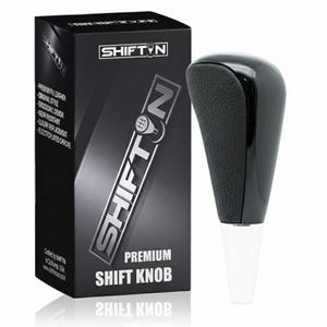 May include: A black shift knob with a textured grip and a glossy top, next to a black box with the brand name SHIFT'N. The box also displays product features like "Premium PU Leather" and "Ergonomic Design."