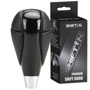 May include: Black leather gear shift knob with a chrome accent and a perforated design. The knob is packaged in a black box with the brand name "SHIFT'N" and the text "PREMIUM SHIFT KNOB".
