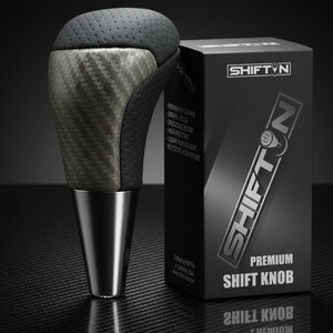 May include: A premium shift knob with a carbon fiber and black leather design. The knob has a silver base and is next to a black box with the "SHIFT N" logo and "PREMIUM SHIFT KNOB" text.