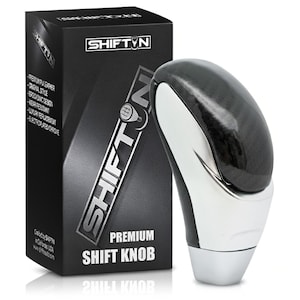 May include: A premium shift knob with a black and silver design, next to a black box with the text "SHIFTIN" and product details. The shift knob has a glossy black top and a silver base.