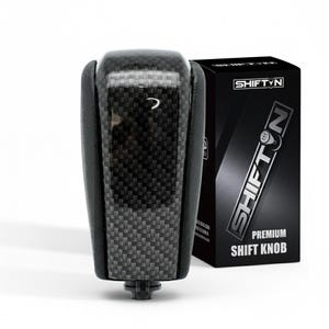 May include: A black and gray shift knob with a carbon fiber weave pattern. The shift knob is next to a black box with the text "SHIFTN" and "PREMIUM SHIFT KNOB" in white.