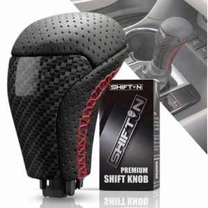May include: A black gear shift knob featuring a perforated top section, carbon fiber textured sides, and red stitching along the seams. The product is displayed next to a black box labeled SHIFTN PREMIUM SHIFT KNOB with a logo graphic.