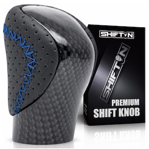 May include: A gear shift knob featuring a black carbon fiber finish and perforated black side panels with blue cross-stitching. Next to it is a black box with the text SHIFTN and PREMIUM SHIFT KNOB printed in white, featuring a gear icon.