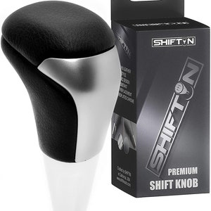 May include: A black and silver shift knob with a white base. The top is black with a textured appearance, and the middle section is silver. The product is packaged in a black box with the text "SHIFT N" and "PREMIUM SHIFT KNOB".