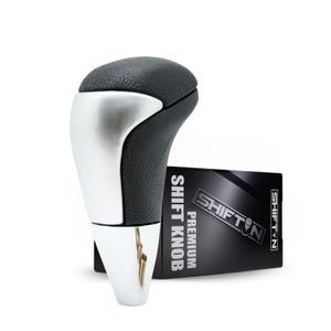 May include: A car shift knob with a black leather top and a silver-colored body. The product is next to a black box with the text "SHIFT KNOB PREMIUM" and the brand name "SHIFTN".