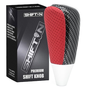May include: A premium shift knob with a carbon fiber and red perforated leather design. The shift knob has a white base and is packaged in a black box with the text "SHIFT N" and "PREMIUM SHIFT KNOB".