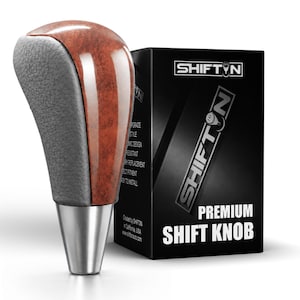 May include: A gear shift knob featuring a polished brown wood grain center panel, textured dark gray side grips, and a silver metallic base. It is displayed next to a black product box labeled SHIFTN PREMIUM SHIFT KNOB with white text.