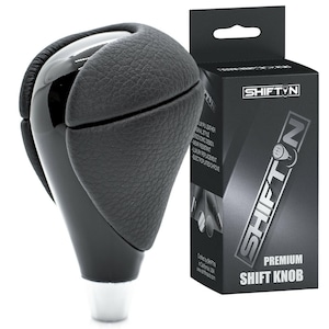 May include: A black premium shift knob with a glossy finish and textured leather grip. The shift knob is next to a black box with the text "SHIFT N" and "PREMIUM SHIFT KNOB". The shift knob has a white base.