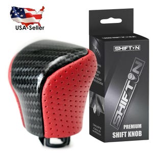 May include: A premium shift knob with a carbon fiber and red leather design. The shift knob has a black base and is packaged in a black box with the "SHIFTN" logo and product information.