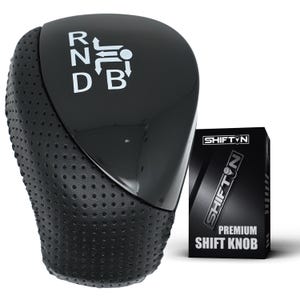 May include: A black gear shift knob with a glossy top surface featuring white R, N, D, B lettering and a directional diagram. The sides are textured with a perforated pattern. Next to it is a black box labeled SHIFTON PREMIUM SHIFT KNOB.