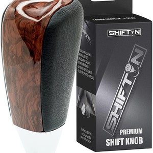May include: A brown wood and black leather shift knob with a chrome base. The knob is labeled "SHIFTIN PREMIUM SHIFT KNOB".