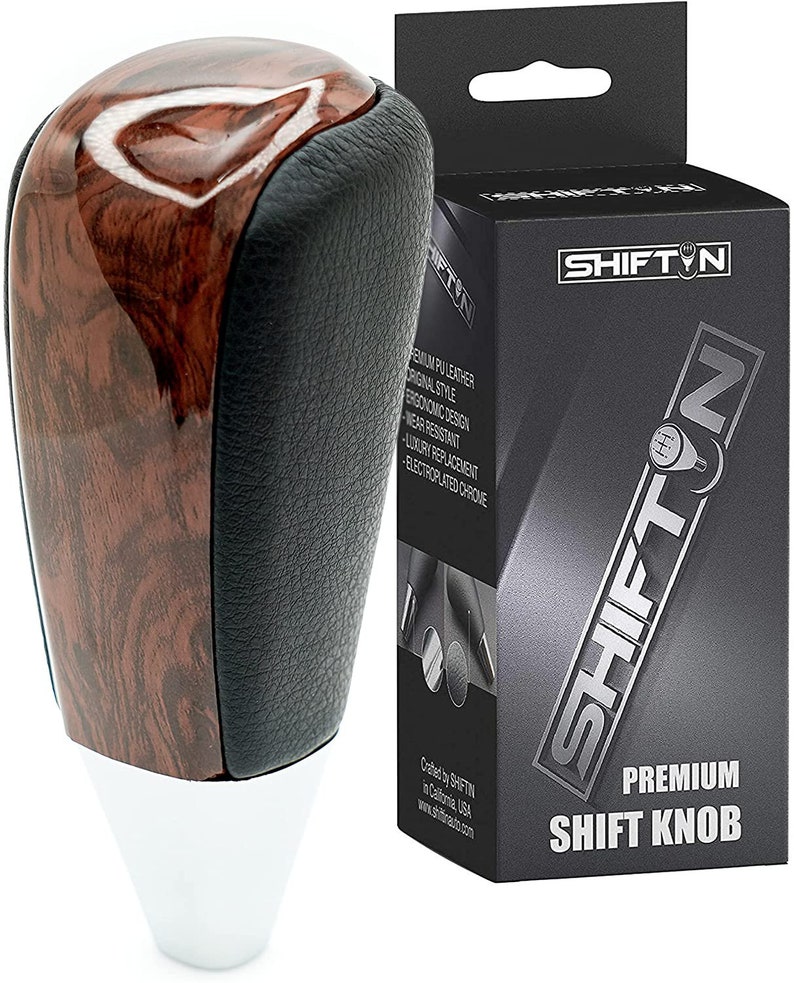 May include: A brown wood and black leather shift knob with a chrome base. The knob is labeled "SHIFTIN PREMIUM SHIFT KNOB".
