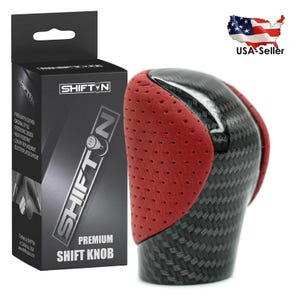 May include: A premium shift knob with a carbon fiber and red leather design. The shift knob is black with a red perforated leather grip. The box next to it has the brand name SHIFT N and the words "Premium Shift Knob".