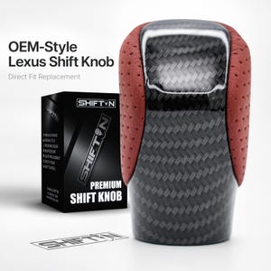 May include: A gear shift knob featuring a central carbon fibre pattern panel flanked by perforated red side sections. The product is displayed next to its black packaging box, which is labelled with the text SHIFTN PREMIUM SHIFT KNOB.