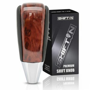 May include: A premium shift knob with a wood grain top, black leather sides, and a chrome base. The shift knob is next to a black box with the brand name "SHIFTN" in white and silver lettering. The box also says "PREMIUM SHIFT KNOB".