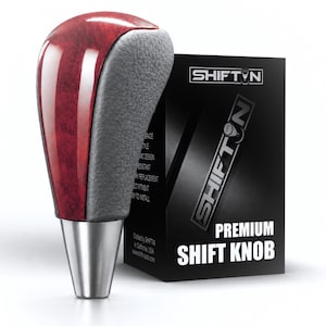 May include: A gear shift knob featuring a glossy red wood-grain center panel flanked by textured grey leather-like sides and a metallic silver base. It is displayed next to a black product box labeled SHIFTN PREMIUM SHIFT KNOB with white text.