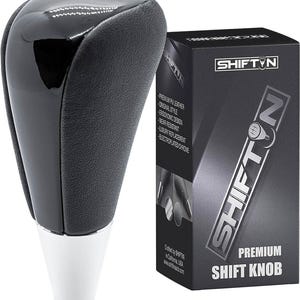 May include: A black and silver shift knob with a glossy top and textured sides. The product is next to a black box with the text "SHIFTIN" and "PREMIUM SHIFT KNOB". The box also lists features like "PREMIUM PU LEATHER".