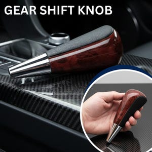 May include: A gear shift knob featuring a dark brown wood grain finish on the sides, a black textured top, and a polished silver metallic base. The text GEAR SHIFT KNOB is displayed at the top of the image, and a circular inset shows the knob.