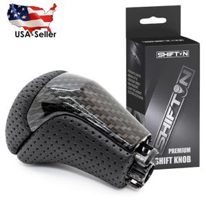 May include: A black and carbon fiber premium shift knob with a perforated leather grip. The product is displayed with its packaging, which features the brand name "SHIFTYN" and product details. The image also includes a USA seller graphic.