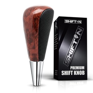 May include: A gear shift knob featuring a polished wood grain finish on the front and a textured black grip on the back, with a silver metallic base. It is displayed next to a black box labeled SHIFTON PREMIUM SHIFT KNOB with white text.