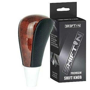 May include: A premium shift knob with a wood grain top and black leather sides. The knob has a white base and is next to a black box with the text "SHIFTN" and "PREMIUM SHIFT KNOB".