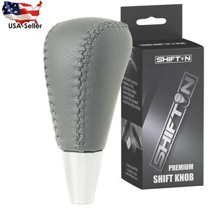 May include: Gray leather shift knob with white base and stitched detailing. The product is packaged in a black box with the text "SHIFT N PREMIUM SHIFT KNOB". The product is a USA Seller.