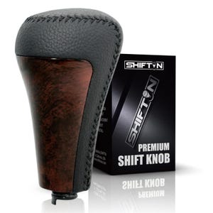 May include: A gear shift knob featuring a black textured leather top with visible stitching and a dark brown wood grain finish on the sides. The product is displayed next to a black box labeled SHIFTIN Premium Shift Knob with white text.