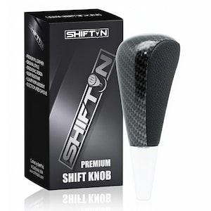 May include: A carbon fiber shift knob with a black leather grip and a white base. The product is displayed next to a black box with the text "SHIFT N" and "PREMIUM SHIFT KNOB".