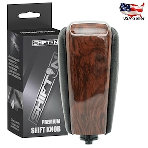 May include: A premium shift knob with a wood grain finish and black leather accents. The product is from SHIFTIN and is a luxury replacement. The box includes the text "PREMIUM SHIFT KNOB".