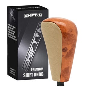 May include: A premium shift knob with a wood grain finish and tan leather accents. The product is packaged in a black box with the "SHIFTIN" logo and product details. The text "PREMIUM SHIFT KNOB" is visible on the box.