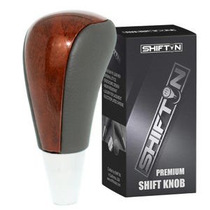 May include: A premium shift knob with a wood grain top, gray sides, and a white base. The product is packaged in a black box with the text "SHIFT N" and "PREMIUM SHIFT KNOB". The box also lists features like ergonomic design.