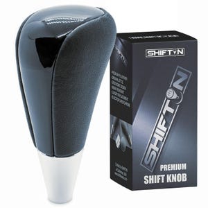 May include: A black and silver shift knob with a glossy top and textured sides. The shift knob is next to a black box with the text "SHIFT N" and "PREMIUM SHIFT KNOB". The box also lists features like "Original Style" and "Wear Resistant".