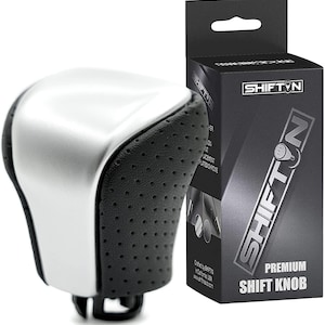 May include: Silver and black shift knob with a perforated leather grip. The knob is a replacement for a standard shift knob and is designed to improve the feel and look of a car's interior. The knob is made by Shift'N and is labeled "Premium Shift Knob".