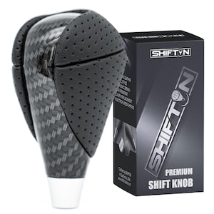 May include: A premium shift knob with a carbon fiber weave pattern and black perforated leather accents. The knob has a white base and is next to a black box with the "SHIFTIN" logo and "PREMIUM SHIFT KNOB" text.