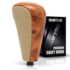 May include: A gear shift knob featuring a polished wood grain finish on the sides and a textured beige leather insert on the front. Beside it stands a black rectangular box labeled SHIFTON PREMIUM SHIFT KNOB with a white logo and text.