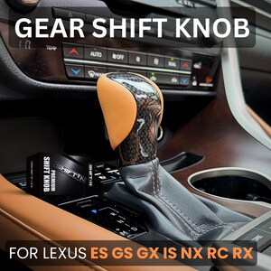 May include: A gear shift knob featuring a tan leather side panel and a glossy carbon fibre finish, installed in a vehicle console. The product is accompanied by a black box labelled SHIFT N PREMIUM SHIFT KNOB. Text on the image reads GEAR SHIFT KNOB FOR LEXUS ES GS GX IS NX RC RX.