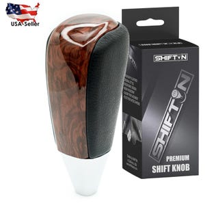 May include: A premium shift knob with a wood grain top, black leather sides, and a white base. The product is packaged in a black box with the "SHIFTN" logo and the words "PREMIUM SHIFT KNOB".