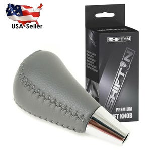 May include: Gray leather shift knob with silver base and stitched detailing. The product is packaged in a black box with the text "SHIFT N" and "PREMIUM SHIFT KNOB". The image also includes a USA seller graphic.
