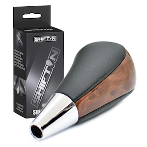 May include: A black and wood grain shift knob with a chrome base, next to a black box with the Shift N logo. The shift knob has a leather top and a wood grain finish on the sides.