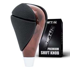 May include: A gear shift knob featuring a textured black leather upper section and a polished brown wood-grain lower body with a silver base. The product is displayed next to a black box labeled SHIFTON PREMIUM SHIFT KNOB in white text.