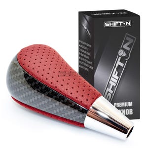 May include: A red and black shift knob with a perforated leather top and carbon fiber accents. The knob has a chrome base and the text "SHIFTIN" is visible on the packaging. The product is labeled as a "PREMIUM KNOB".