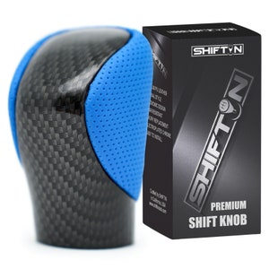 May include: A black and blue carbon fiber shift knob with a perforated blue leather insert. The knob is packaged in a black box with the brand name "SHIFT'N" and the text "PREMIUM SHIFT KNOB".