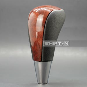 May include: A car gear shift knob with a wood grain top and a black leather grip. The base is silver. The text "SHIFT N" is visible on the side.