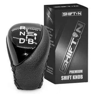 May include: Black and silver shift knob with a leather grip and a glossy top displaying gear shift symbols. The product is accompanied by a black box with the text "SHIFT N" and "PREMIUM SHIFT KNOB".